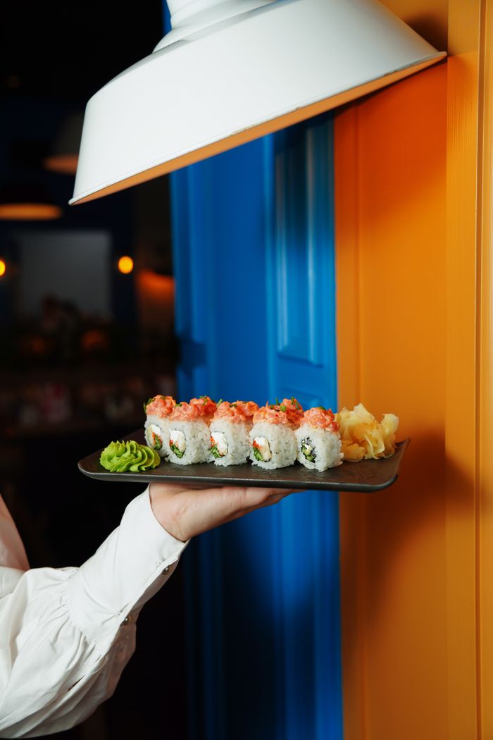 contact-img Close-up of a sushi platter served by a waiter against a bold, colorful background.