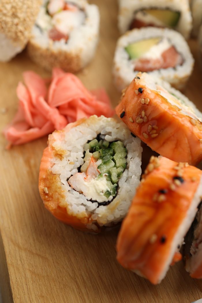services-01 Close-up of delicious sushi rolls with rice, seafood, and sesame seeds on a wooden board.