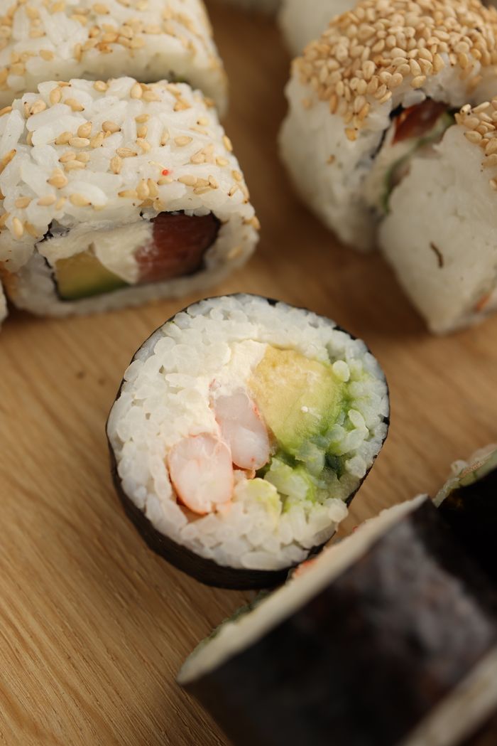 services-01 Close-up of sushi rolls featuring fresh avocado and seafood on a wooden board.