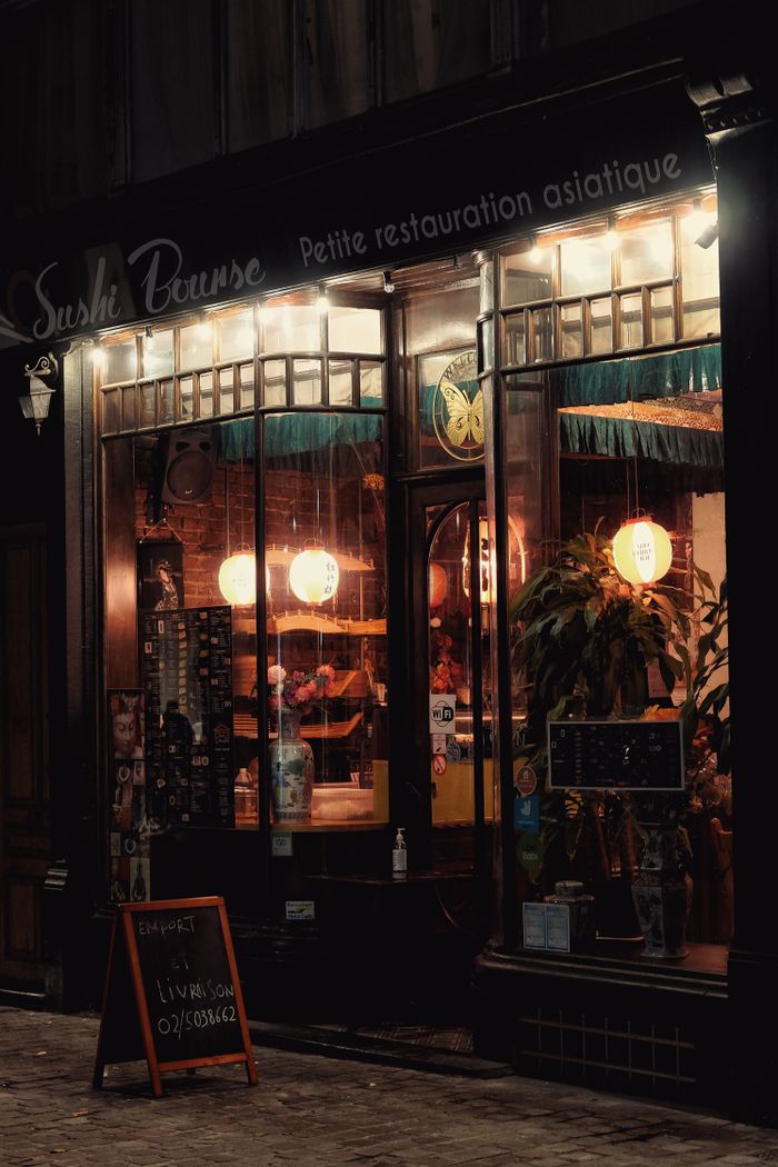 Charming sushi restaurant facade in Brussels illuminated at night, showcasing a cozy and inviting atmosphere.